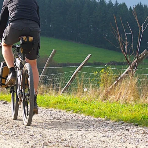 cycliste sur son vélo titane gravel titane bikepacking outquest obvious qui roule sur un chemin de pierre. la vue est prise de dos.